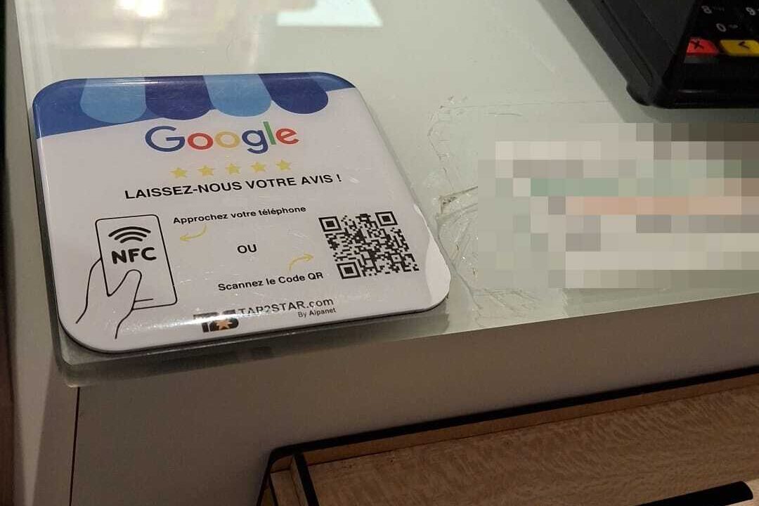 Plaque avis Google Tap2Star posée à plat sur le comptoir vitré de la Pharmacie Moderne, à gauche du terminal de paiement, avec sa zone NFC et son QR code.